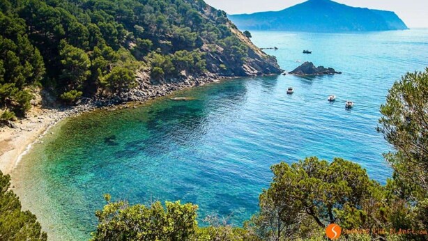 A coastal landscape with clear blue waters, rocky shores, and dense greenery.