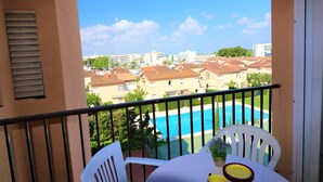 A balcony with a table and chairs, overlooking a swimming pool and residential buildings.