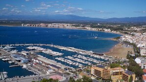 A marina with numerous boats docked, a sandy beach, and a coastal cityscape with buildings.