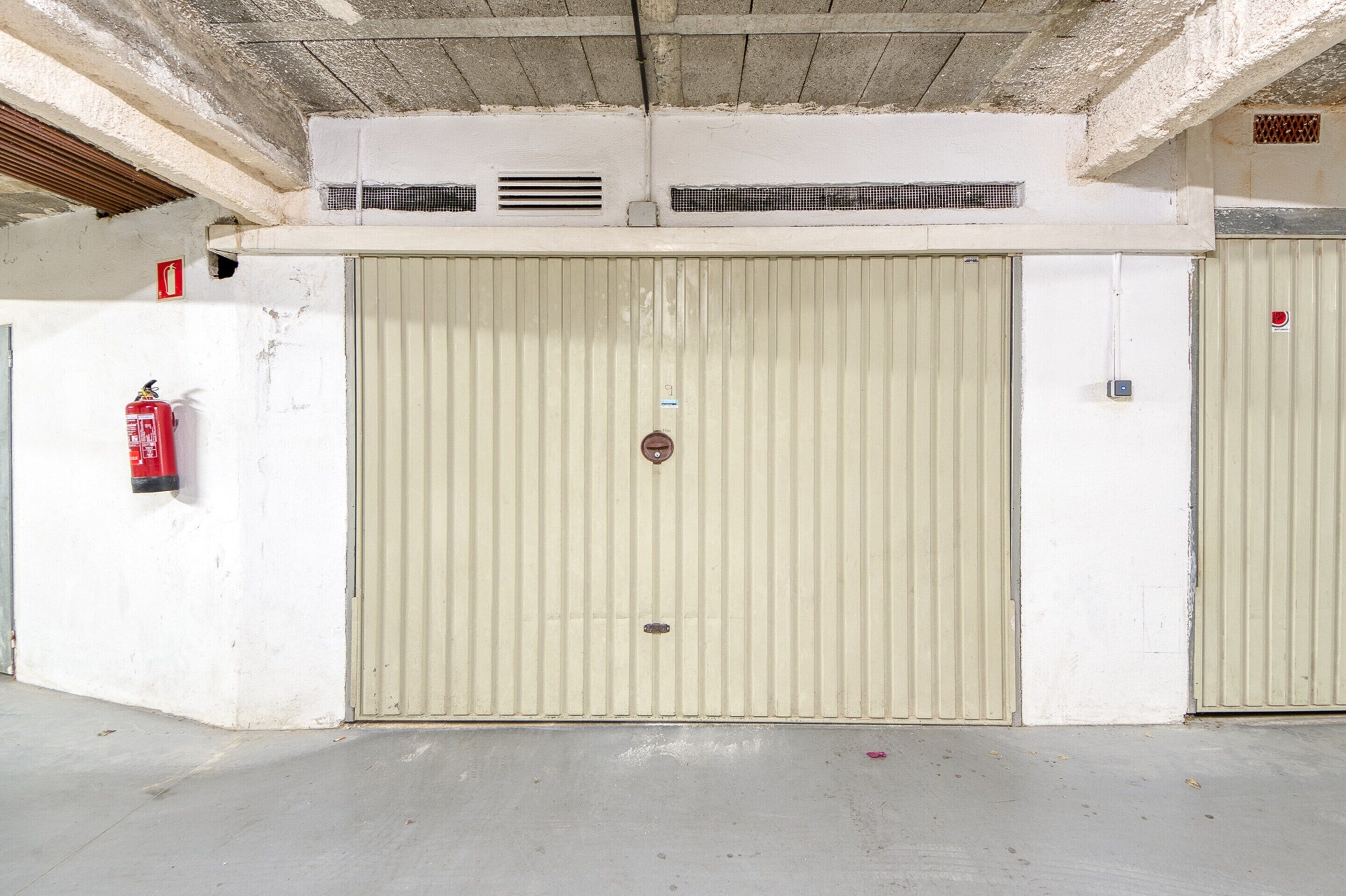 A closed, beige metal door with a fire extinguisher mounted on the wall to its left.