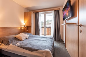 Una habitación de hotel moderna con una cama grande, un televisor montado en la pared y un ventanal corredero que da a un balcón.