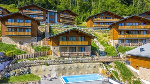 A cluster of wooden chalet-style buildings with balconies, a swimming pool, and a stone retaining wall. - Chalet in Wagrain Near the Flying Mozart (Wagrain)