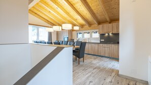 A modern kitchen with wooden beams, a dining area with a long table, and a view of the outdoors. - Chalet in Wagrain Near the Flying Mozart (Wagrain)
