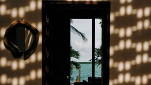 A doorway leading to a beach view with palm trees and water. - Ik Casa Del Viento  (Chetumal)