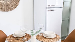 Een eetgedeelte met een ronde marmeren tafel, twee bruine leren stoelen, een witte koelkast en een decoratief wandkunstwerk.