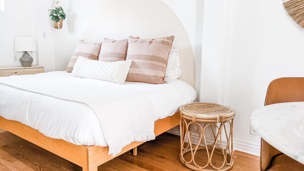Een slaapkamer met een houten bed, witte beddengoed en een rieten kruk.