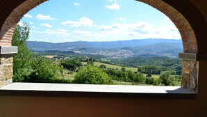 A view through a brick arch window overlooking a valley with distant mountains and greenery. - Farmhouse in Tuscany With Pool and Valley Views (Poppi)