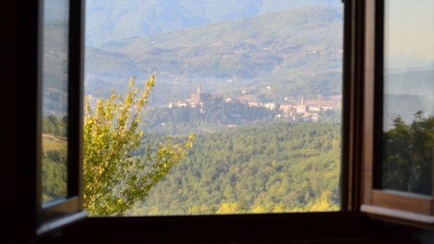 A view through a window of a town nestled in a valley with mountains in the background. - Farmhouse in Tuscany With Pool and Valley Views (Poppi)