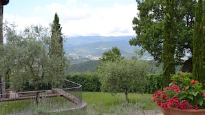 A garden with a circular metal railing, a large terracotta pot with red flowers, and a view of distant mountains. - Farmhouse in Tuscany With Pool and Valley Views (Poppi)