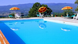 A swimming pool with clear blue water, surrounded by lounge chairs and umbrellas, with a mountainous backdrop. - Farmhouse in Tuscany With Pool and Valley Views (Poppi)