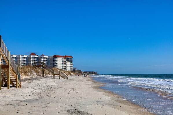Ein Strand mit Holzstegen, die zu einer Reihe mehrstöckiger Gebäude mit roten Dächern führen.