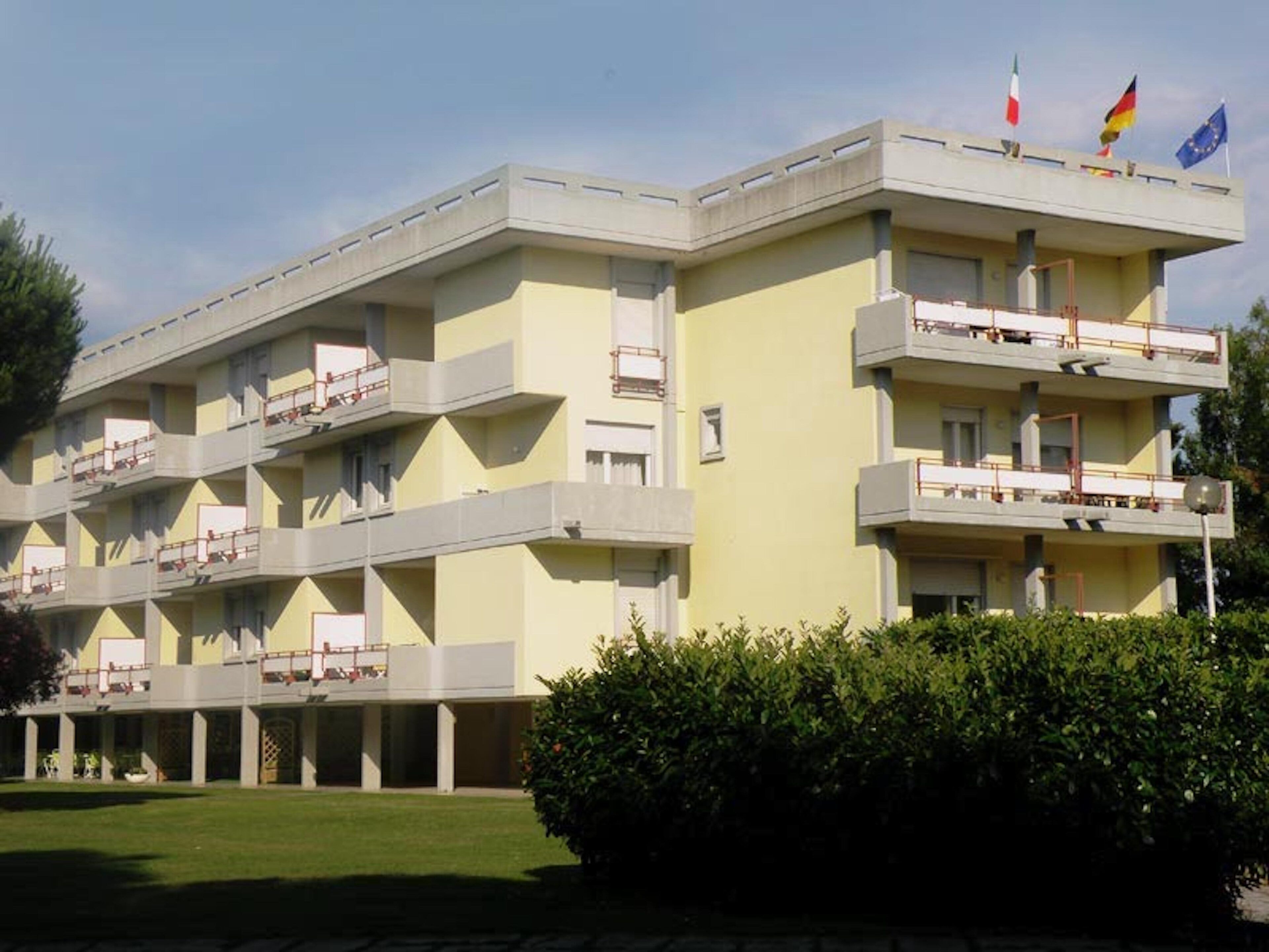 A multi-story building with balconies, flags, and a well-maintained lawn.
