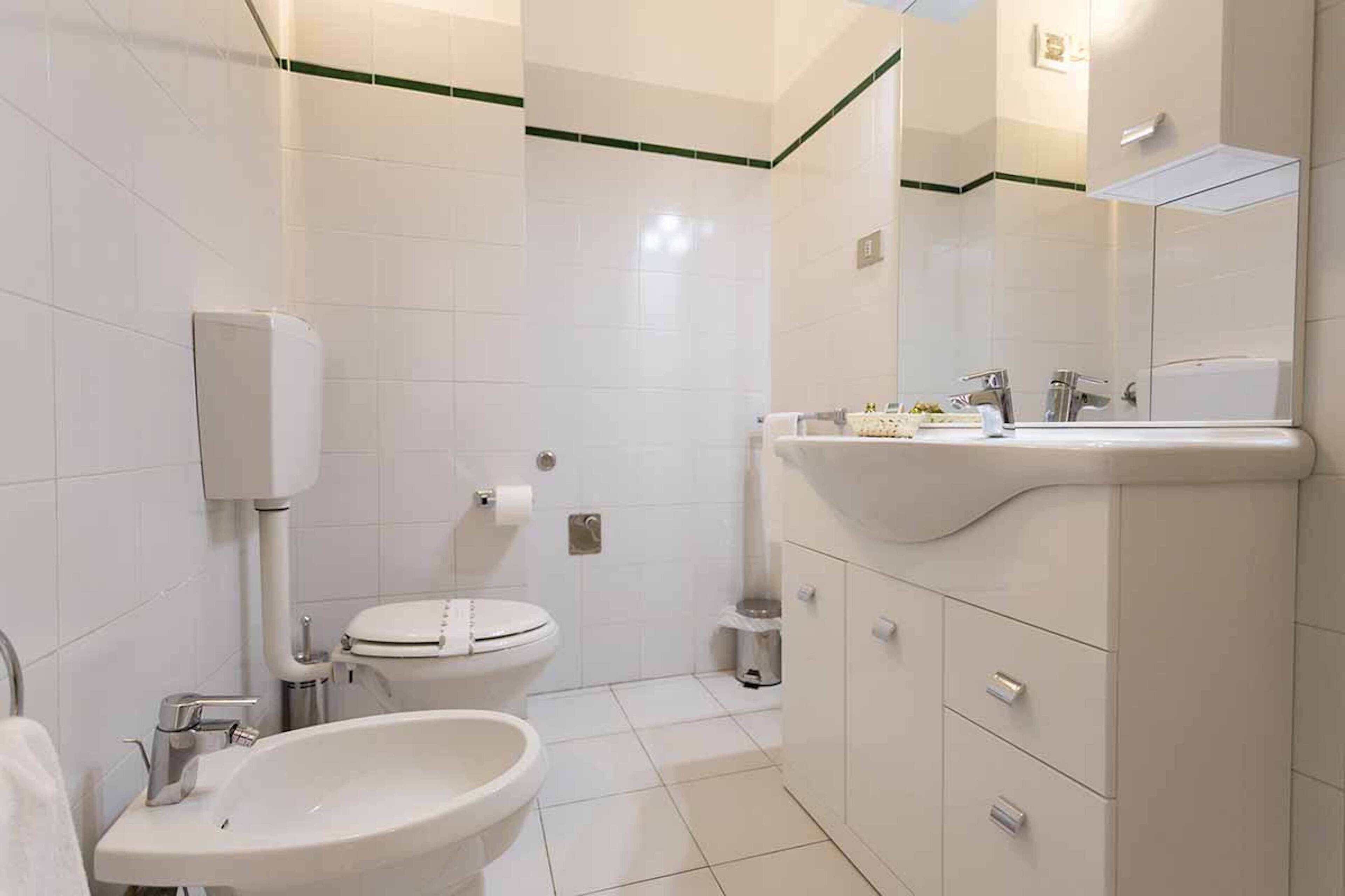 Een moderne badkamer met witte tegels, een wastafel, toilet en spiegel.