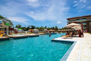 Ein Schwimmbeckenbereich mit mehreren Pools, Liegestühlen, Sonnenschirmen und einem Spielplatz.
