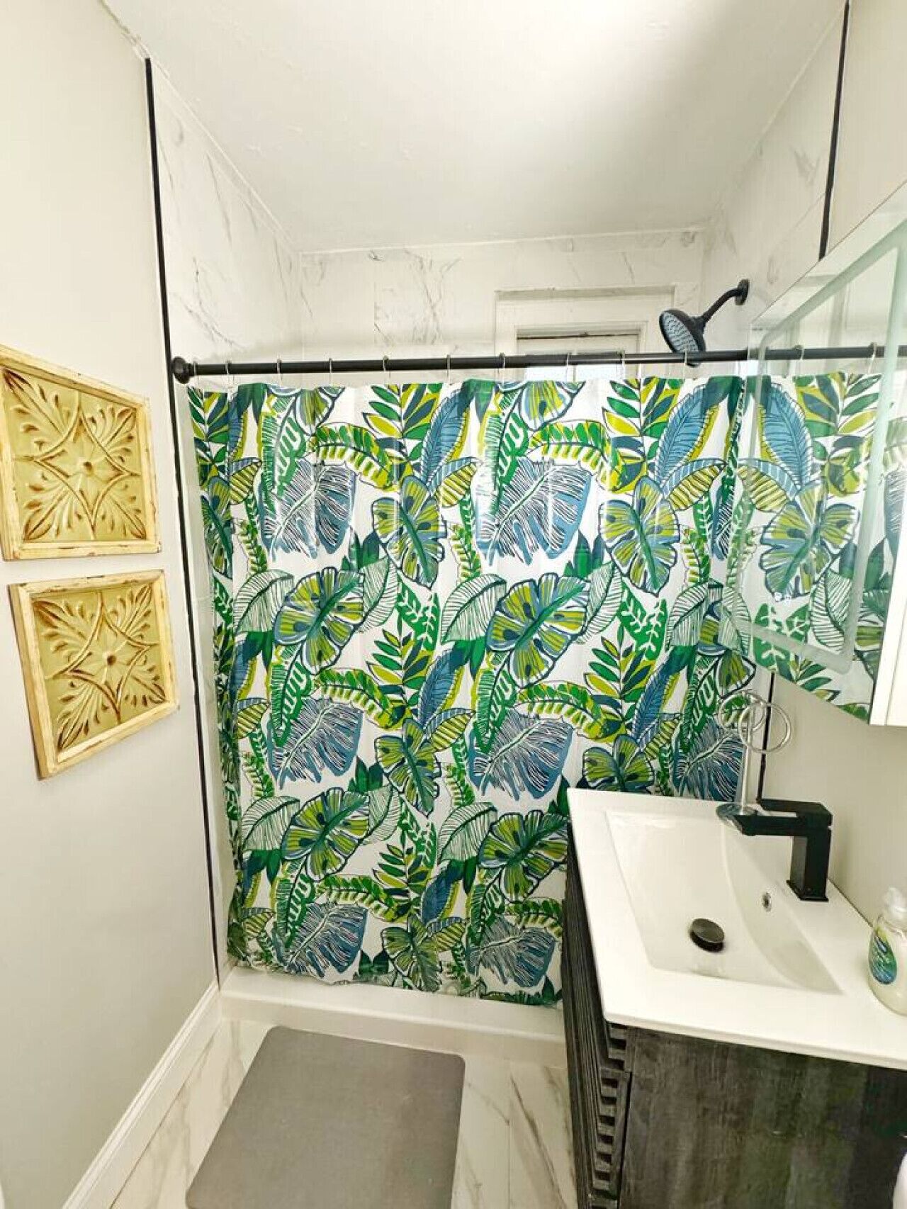 A bathroom with a shower curtain featuring a tropical leaf pattern, a sink with a soap dispenser, and two decorative wall panels.