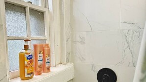 Een badkamer met een douche, een raam en toiletartikelen op de vensterbank.