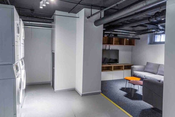 Un interior moderno con un sofá gris, una mesita naranja pequeña y un televisor sobre una estantería de madera.