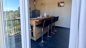 Une cuisine moderne avec un îlot central en bois, des tabourets de bar, un éclairage suspendu et une vue sur l’extérieur.