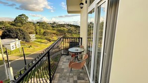 Un balcon avec une table et des chaises, une vue sur un paysage verdoyant et un ciel dégagé.