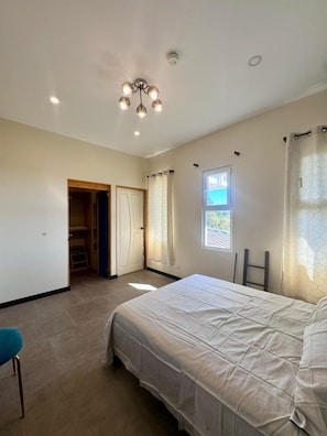 A bedroom with a bed, a wardrobe, a door leading to a closet, and a window with curtains.