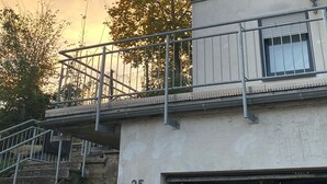 Un edificio con el número 25 en la fachada, una escalera que sube a un balcón, y un árbol con hojas otoñales al fondo.