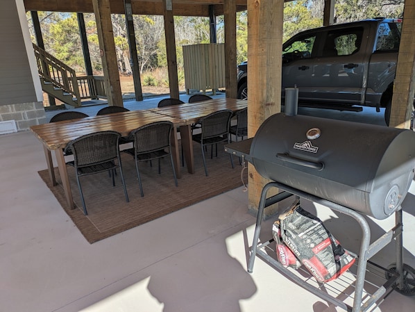 An outdoor patio with a wooden table and chairs, a grill, and a covered staircase.