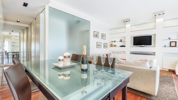 A modern living room with a glass dining table, a sofa, and a flat-screen TV mounted on the wall. - Modern Apartment in Porta Nuova, Milan

 (Milano)