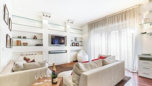 A modern living room with a sofa, a coffee table with glasses and a bottle, a TV on a stand, and a glass shelf unit. - Modern Apartment in Porta Nuova, Milan

 (Milano)