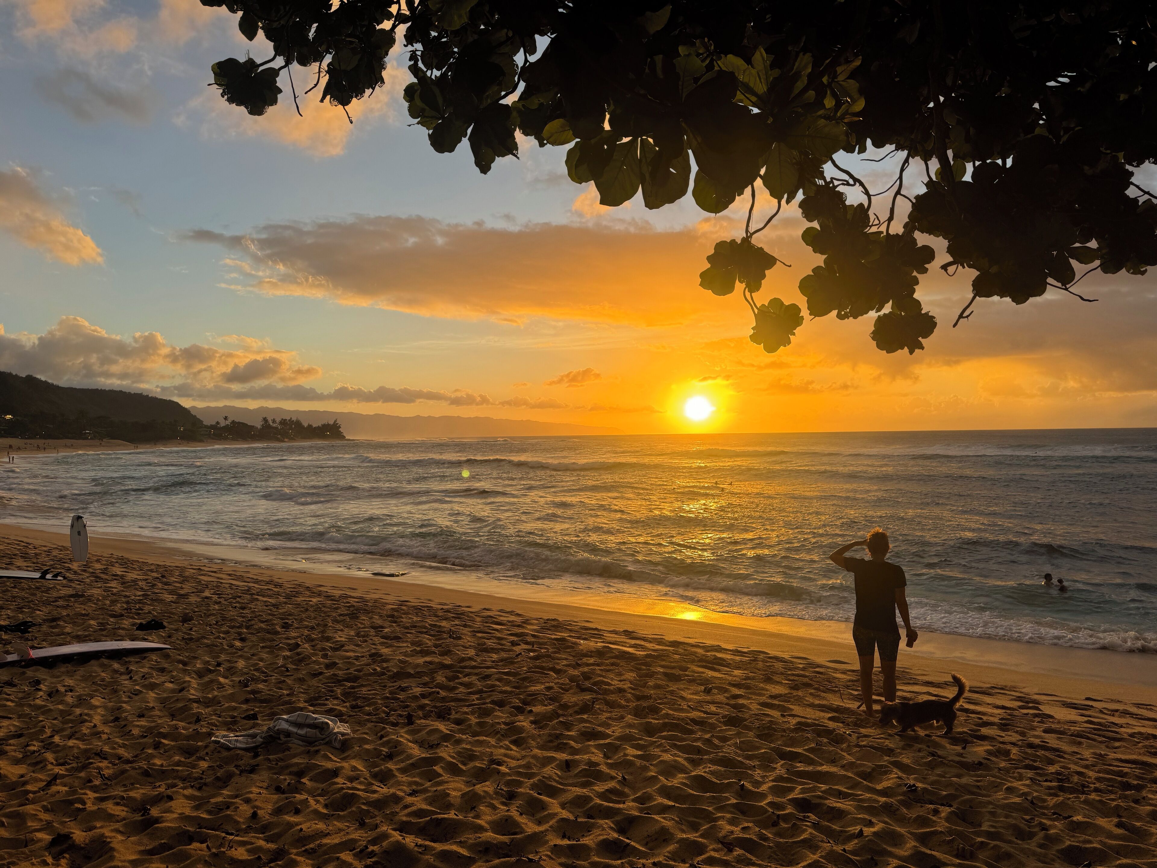 Ein Strand mit Sonnenuntergang, Wellen und einer Person, die im Sand steht.