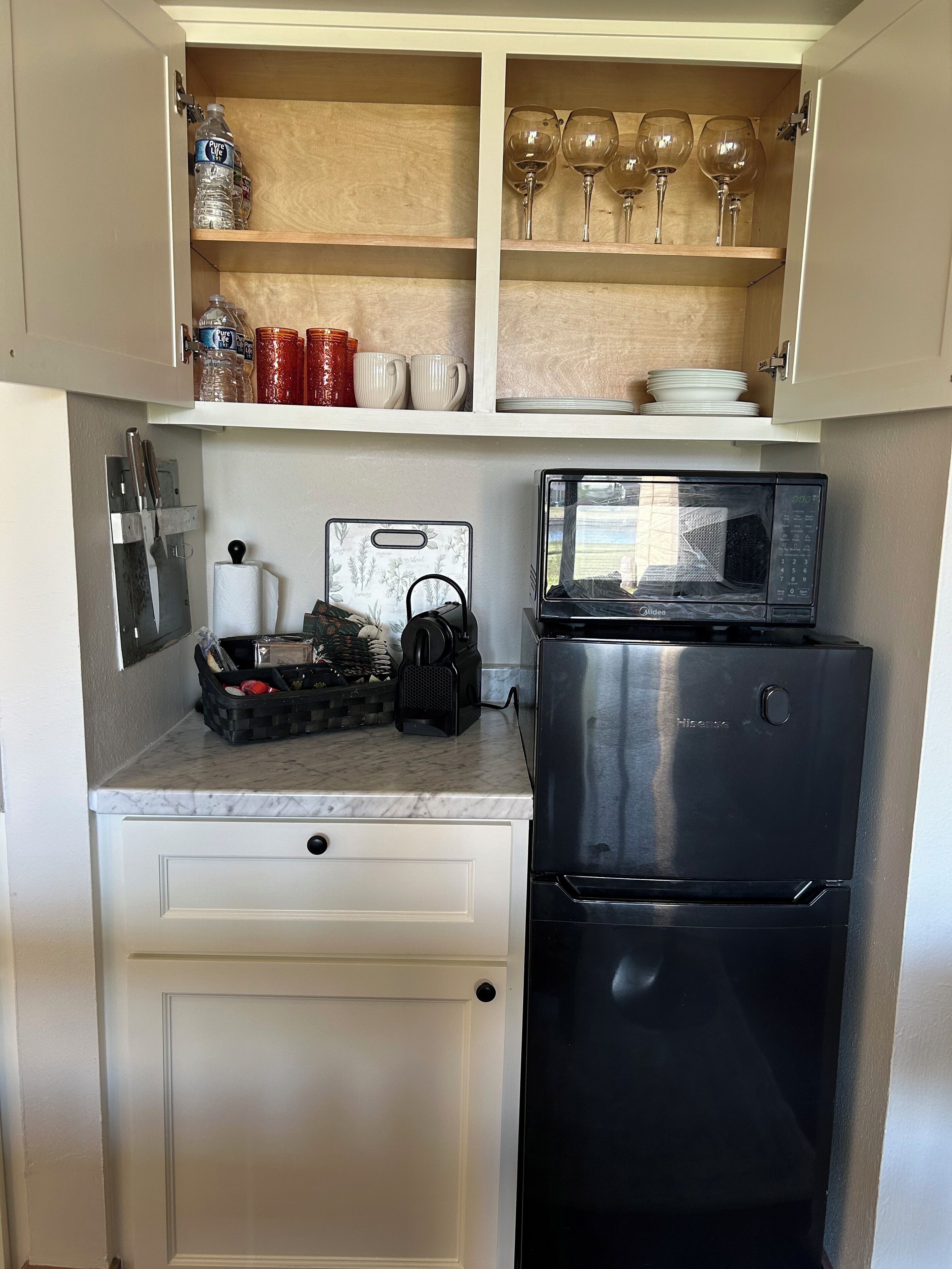 A compact kitchen with a microwave, a refrigerator, and a countertop with a basket and a kettle.