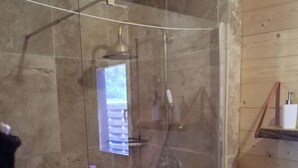 Une douche fermée par des parois en verre, dotée d’un pommeau de douche à main et d’un robinet mural.