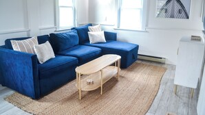 En moderne stue med en blå modulsofa, et træbord og et stort vindue, der lukker naturligt lys ind.