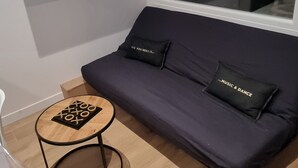 A modern living room with a purple sofa, two black cushions, a small wooden table with a board game, and a large window.