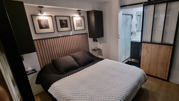A modern bedroom with a bed, a headboard, framed pictures, a nightstand, and a sliding door leading to a bathroom.