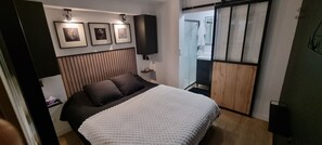 A modern bedroom with a bed, a headboard, framed pictures, a nightstand, and a sliding door leading to a bathroom. - ROMY at thelna (Bray-Dunes)