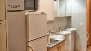 A kitchen with a microwave on top of a refrigerator, a sink, and a mirror above the sink. - Tokyo Vibes Hostel with more privacy (Self Check in) (Vilnius)