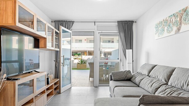 Una sala moderna con un sofá gris, armarios de madera y un televisor.