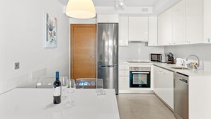 Una cocina moderna con armarios blancos, electrodomésticos de acero inoxidable y un comedor con una mesa dispuesta para dos.