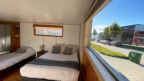 A room with two beds, a window with a view of the street, and a wooden ceiling.