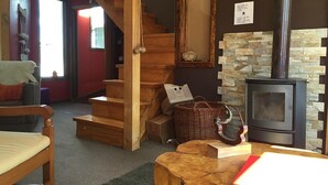 A cozy living room with a wooden staircase, a stone fireplace, and a comfortable seating area. - HOSTAL AMERINDIA (Natales)
