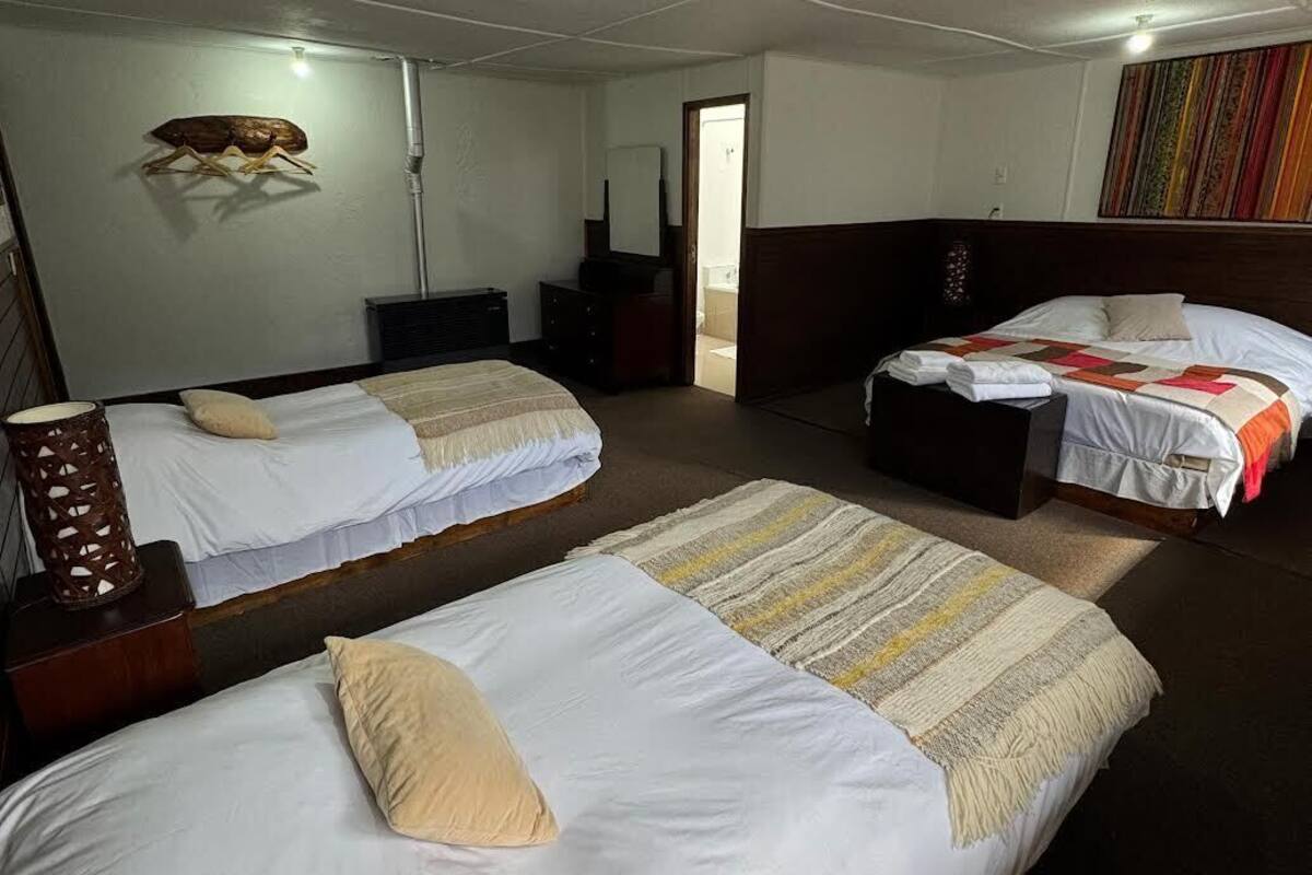 Habitación de hotel con dos camas individuales, cabecera de madera, espejo, cómoda de madera y cortina colorida.
