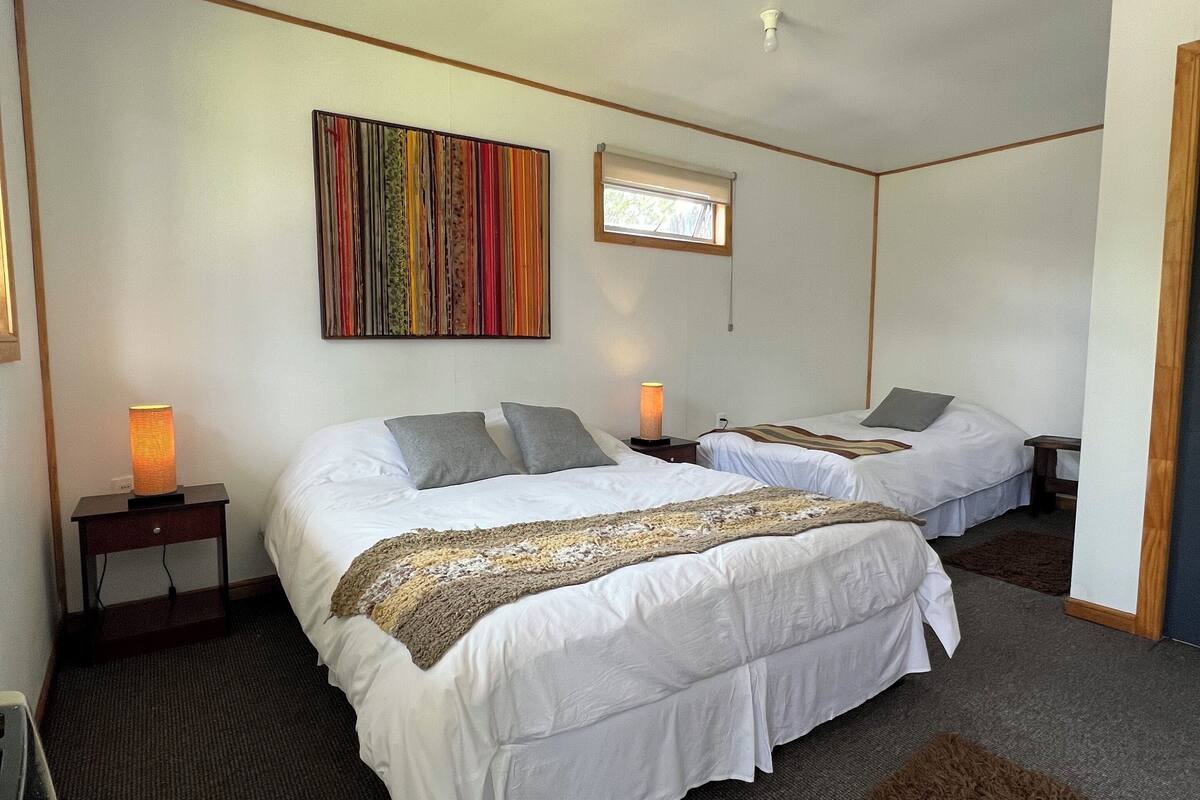 Habitación de hotel con dos camas, un cuadro abstracto de colores, una ventana pequeña y una alfombra marrón.