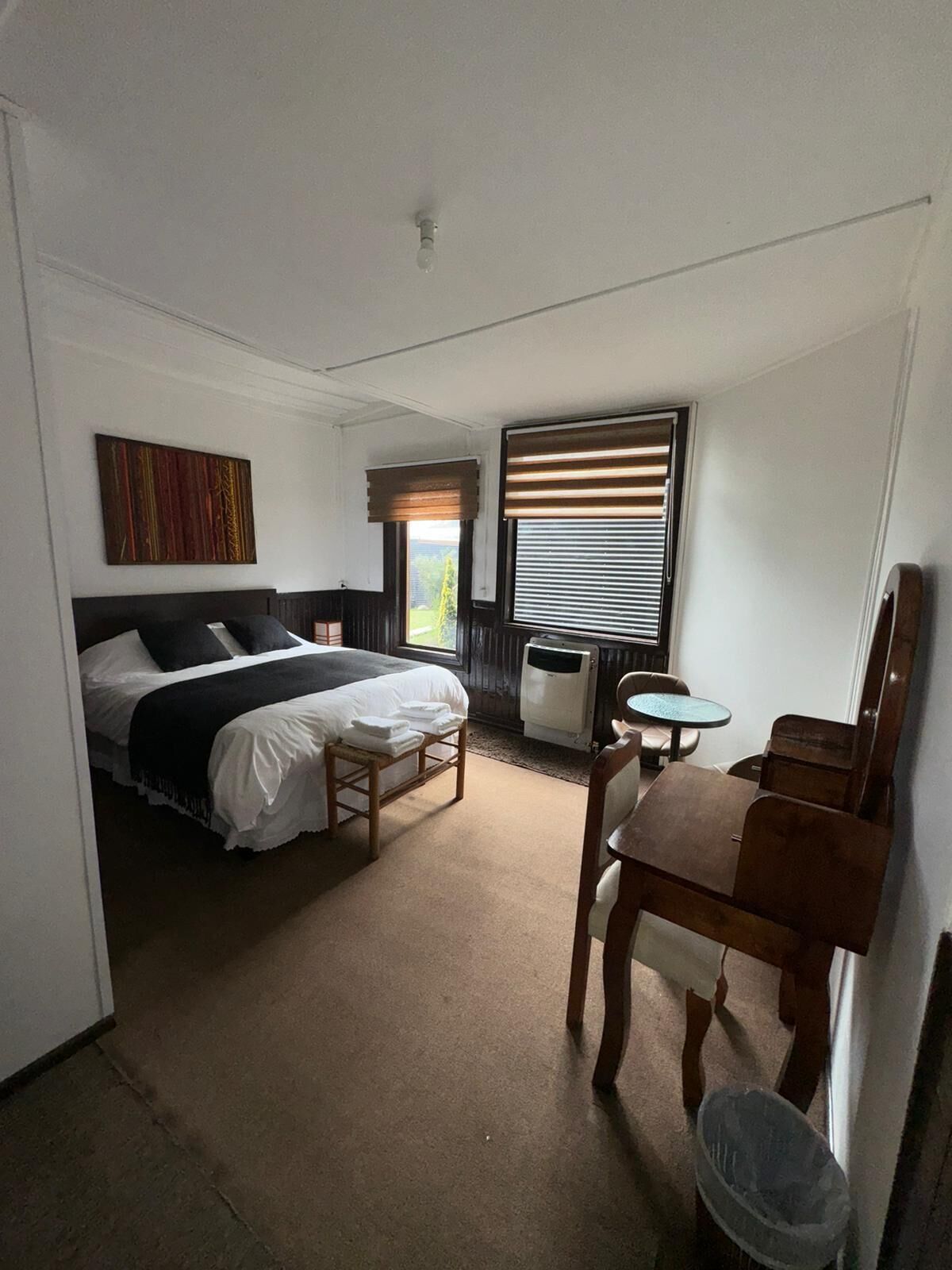 Une chambre d’hôtel équipée d’un lit, d’un bureau, d’une chaise, d’un radiateur et d’une fenêtre avec des stores.