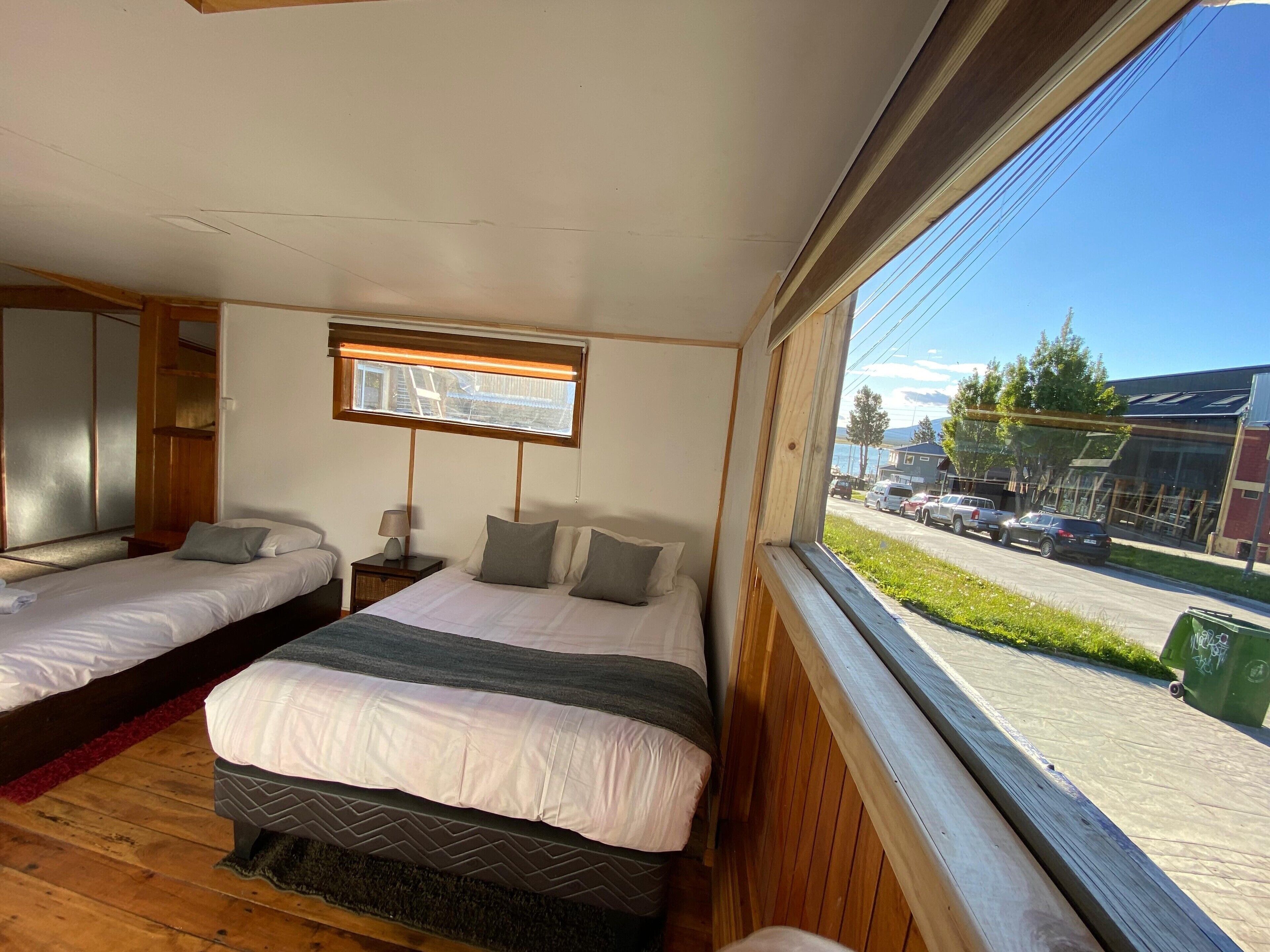 A bedroom with two beds, a window with a view of the street, and a wooden floor.