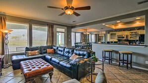 A spacious living room with a large black leather sectional sofa, a brown leather ottoman, and a ceiling fan. - Hole-in-One Vista! (Laguna Vista)