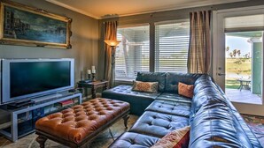 A living room with a large flat-screen TV, leather sofas, and a dining area with a table and chairs. - Hole-in-One Vista! (Laguna Vista)