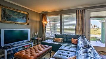 A living room with a large flat-screen TV, leather sofas, and a dining area with a table and chairs.