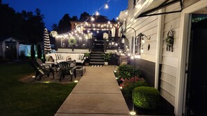 A well-lit outdoor patio area with a concrete pathway leading to a porch, furnished with outdoor seating and decorative lights. - Stylish and Spacious 3 bedroom home located 3.4 mi from downtown Erie, PA (Erie)
