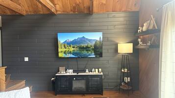 A living room with a mounted TV, wooden ceiling, dark wall, and a small cabinet with decorative items.