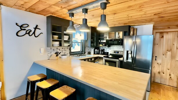 A modern kitchen with a wooden island, bar stools, and a 'Eat' sign on the wall. - Cozy Chalet – Mtn View+ Hot Tub+ Hike+ Santa's Vil (Lancaster)